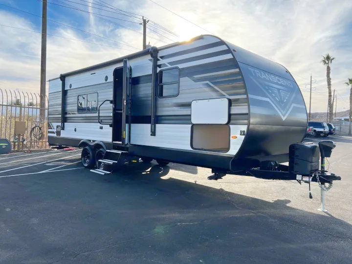 Explore in this new Transcend RV rental, a black, gray, and white travel trailer with open door, parked outdoors.. Grand Design Transcend Xplor 240BH 2022