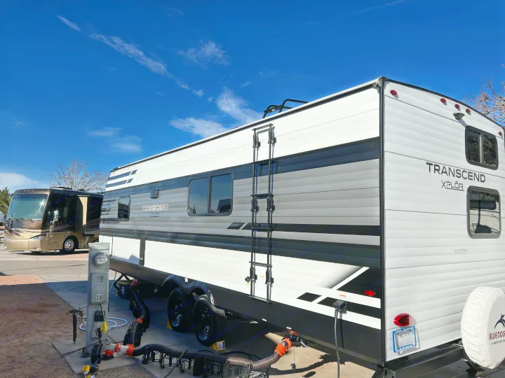 A Grand Design Transcend Xplor travel trailer, potentially an RV rental from Blue Dog RV, is set up at a sunny campground.. Grand Design Transcend Xplor 240BH 2022