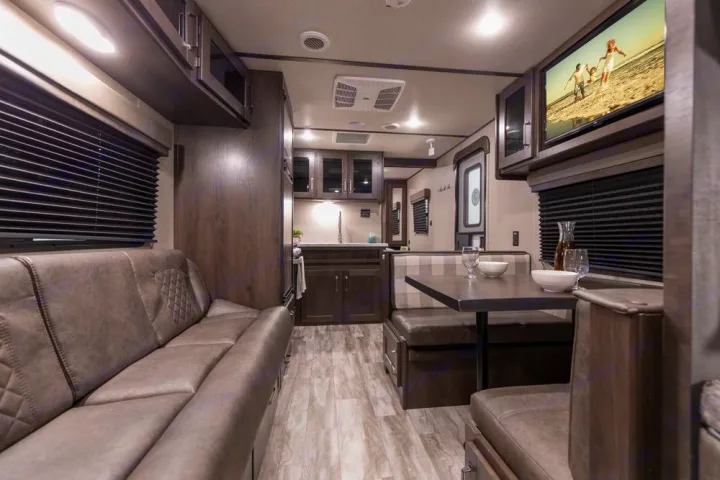 Modern RV rental interior: cozy gray sofa, dark wood cabinetry, and dinette with plaid seating. Spacious living area.. Grand Design Transcend Xplor 240BH 2022