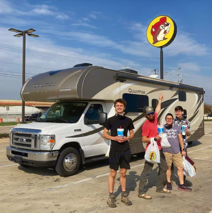 Enjoying a road trip in an RV rental! Four people pose with drinks & bags in front of a large RV & Buc-ee's sign.. Thor Quantum 2017