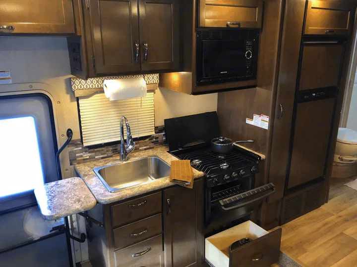 RV rental kitchen: compact space with sink, stove, oven, microwave, fridge, and an open drawer for supplies.. Thor Freedom Elite 2018