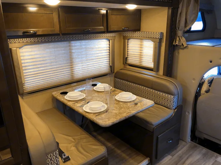 Cozy RV rental interior showing a dining area with set table, overhead cabinets, and bunk for comfortable travel.. Thor Freedom Elite 2018