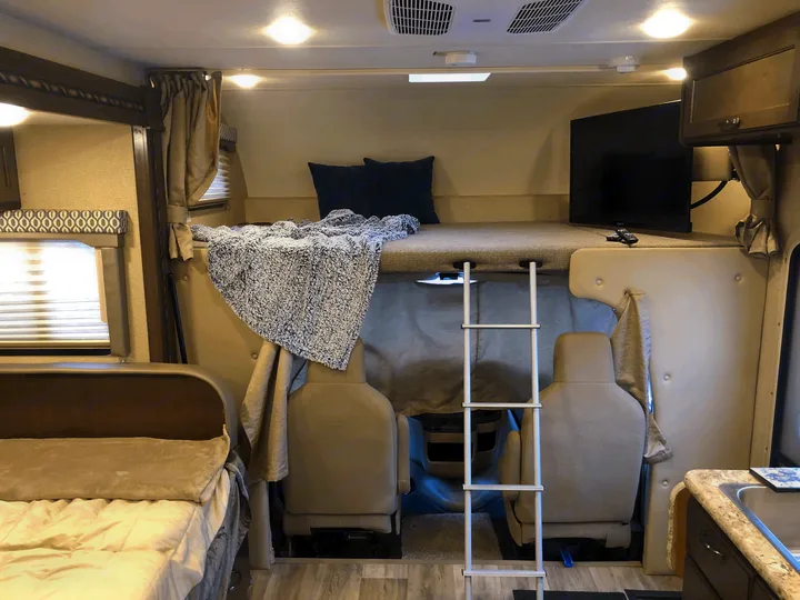 Cozy RV rental interior featuring a cab-over bunk bed with ladder, lounge area, TV, and kitchen sink.. Thor Freedom Elite 2018