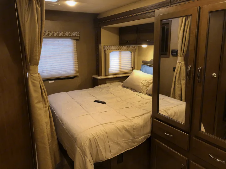 RV rental bedroom: a cozy space featuring a large bed, window blinds, overhead cabinets, and mirrored closet.. Thor Freedom Elite 2018