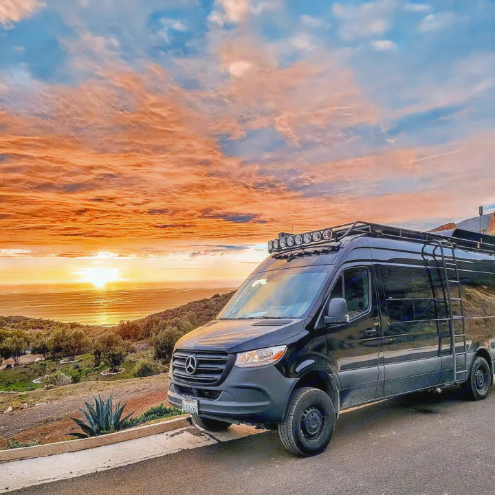 Black Mercedes camper van parked at a scenic ocean overlook during a vivid sunset. Consider this rv rental for your next trip!. Mercedes-Benz Sprinter 2019