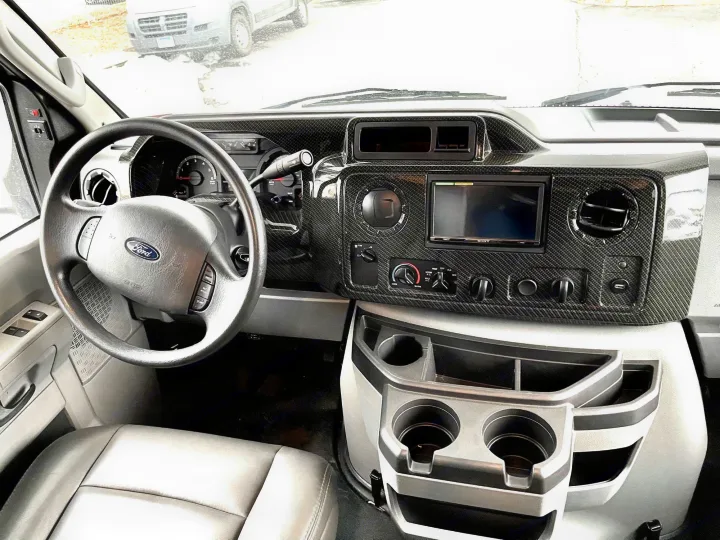 Inside an RV rental: driver's area featuring a Ford steering wheel, carbon-look dashboard with Sony display & cupholders.. Forest River Forester 2020
