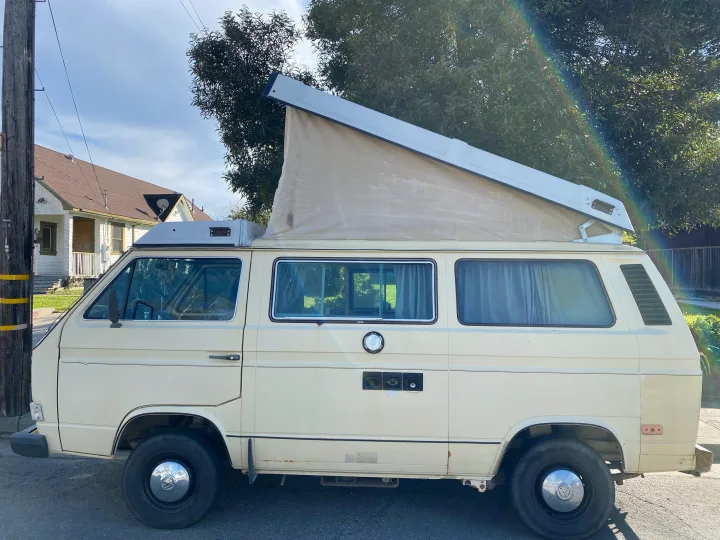 A cream VW Westfalia camper van with pop-top extended, ideal for an RV rental adventure on a sunny day.. Volkswagen Vanagon 1984