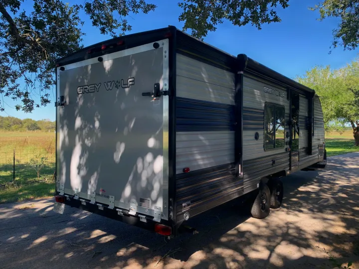 Explore with this Grey Wolf rv rental. A toy hauler travel trailer with a large rear ramp, parked outdoors under trees.. Forest River Cherokee 2021