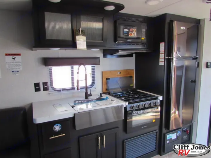 Spacious rv rental kitchen interior with modern black cabinets, sink, gas stove, microwave, and stainless steel fridge.. Forest River Cherokee 2021
