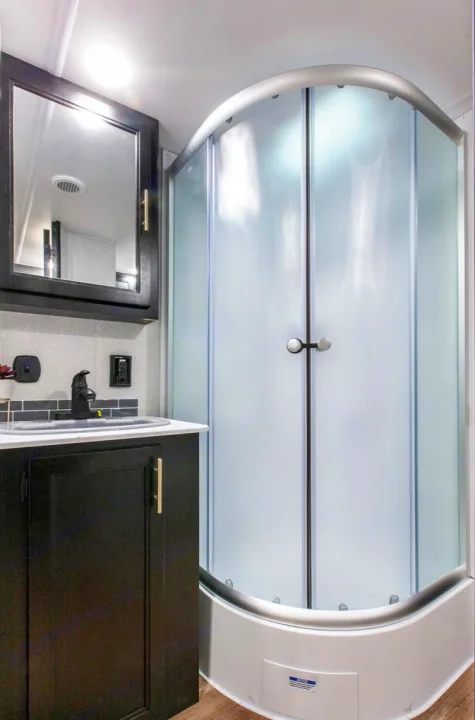 Well-appointed RV rental bathroom featuring a dark vanity, sink, and a compact, curved frosted glass shower stall.. Forest River Cherokee 2021