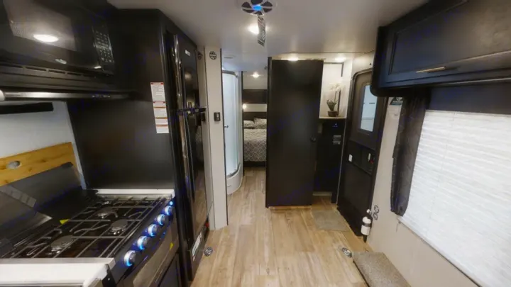 Modern RV rental interior: well-equipped kitchen with stove, microwave, fridge, and a clear hallway leading to the bedroom and shower.. Forest River Cherokee 2021