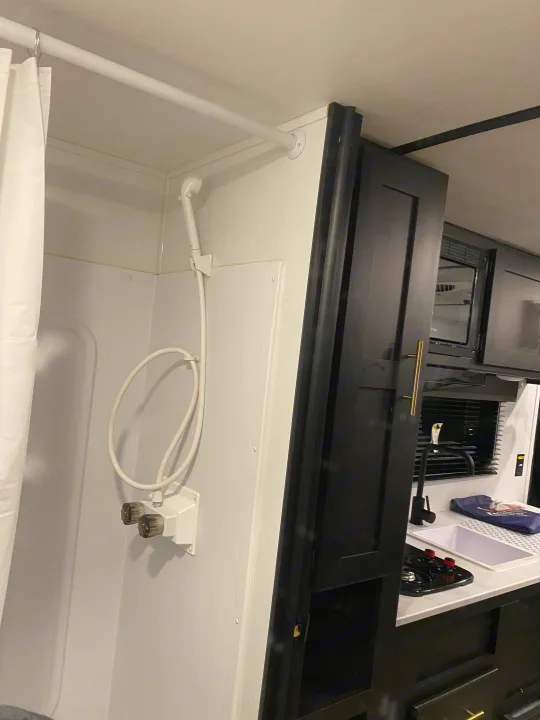 Inside this RV rental, find a clean, compact shower with white fixtures and a modern kitchen with dark cabinetry and a sink.. Keystone Springdale 1800BH 2022