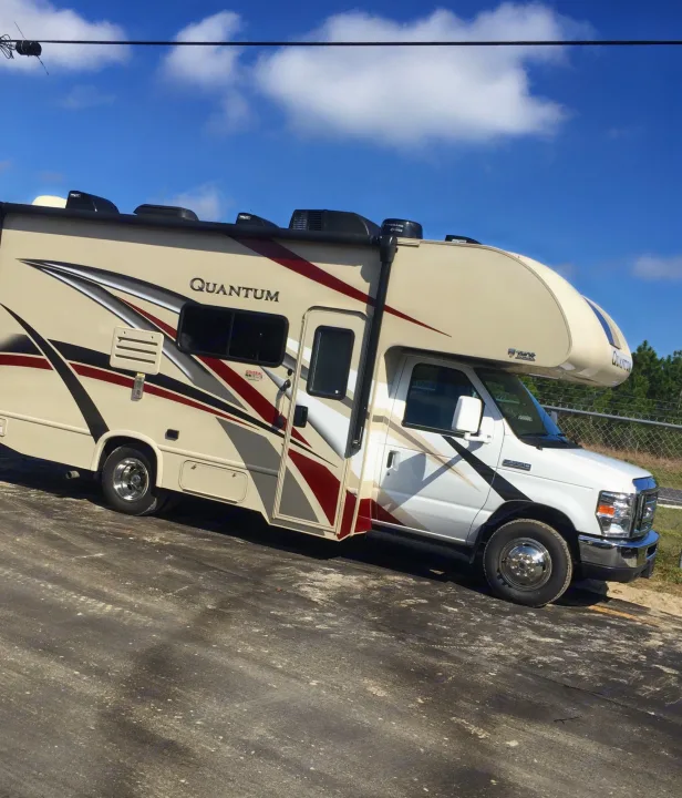 A modern beige and white Quantum Class C motorhome RV rental parked outdoors on a paved surface under a blue sky.. Thor Motor Coach Quantum GR 22 2020