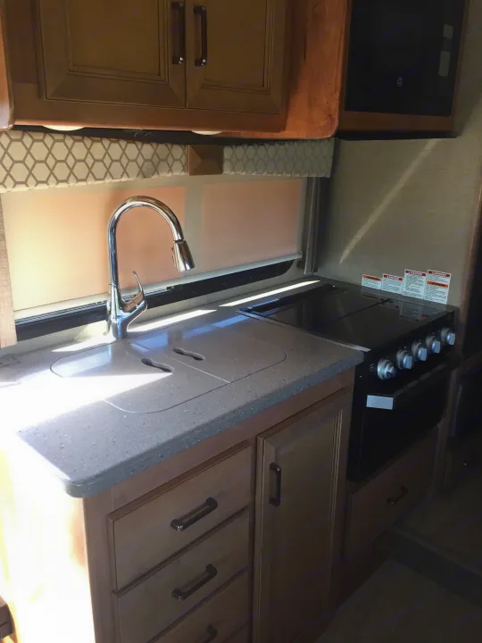 RV rental kitchen: chrome faucet, light countertop, stovetop, oven, microwave, and wood cabinets.. Thor Motor Coach Quantum GR 22 2020