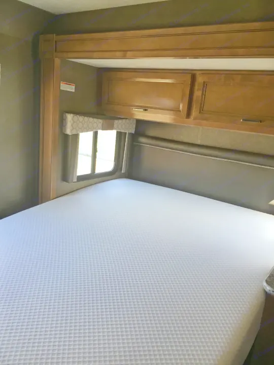 RV rental bedroom showcasing a white, waffle-texture mattress, wood cabinets above, and a window with a valance.. Thor Motor Coach Quantum GR 22 2020