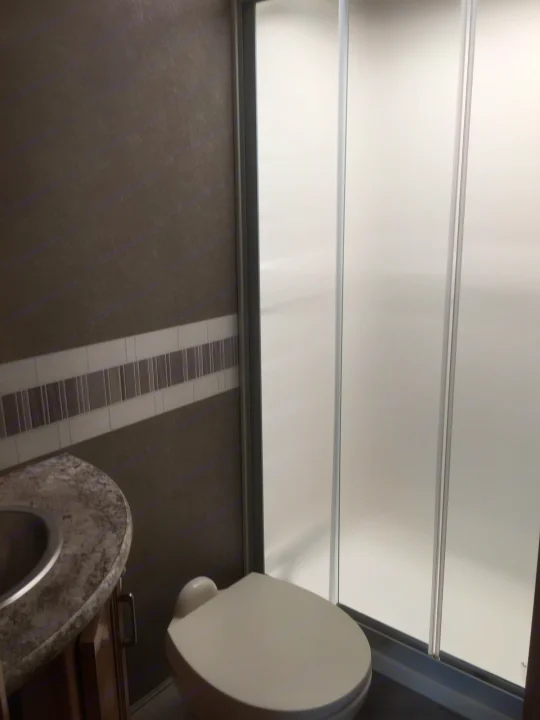 Compact RV rental bathroom featuring a toilet, frosted shower, and vanity with sink. Practical interior for travelers.. Thor Motor Coach Quantum GR 22 2020