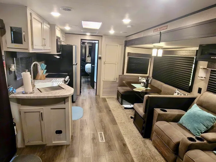 Spacious rv rental interior featuring a modern kitchen, dining booth, living area with recliners, and bedroom entrance.. Jayco Jay Flight 2022