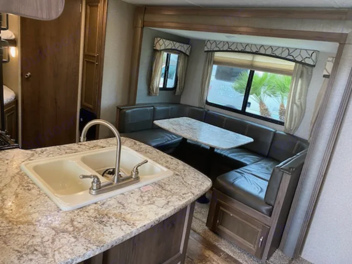Inside a bright RV rental: a kitchen sink island and comfortable U-shaped dinette with large windows. Perfect for road trips!. Keystone Passport 2019