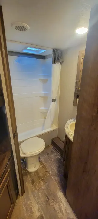 RV rental bathroom with a compact tub/shower, toilet, and sink vanity. Tiled floor and overhead lighting complete the space.. Keystone Passport 2019