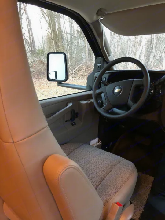 View from an RV rental's passenger seat showing the light beige driver's seat, Chevy steering wheel, and bare trees outside.. Jayco Redhawk 2020