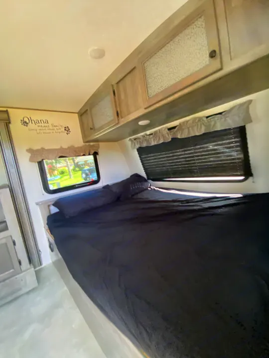 Explore this cozy RV rental bedroom: dark bedding, light wood cabinets, and a window with scenic views. Features an "Ohana" wall decal.. Coachmen Apex Nano 194 BHS 2021