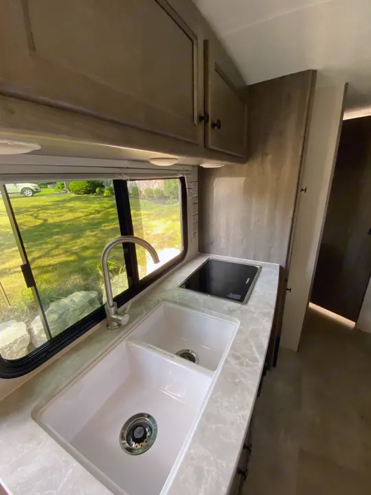 RV rental kitchen featuring a double sink, modern faucet, and cooktop. Overlooking a scenic view, with clean cabinets.. Coachmen Apex Nano 194 BHS 2021
