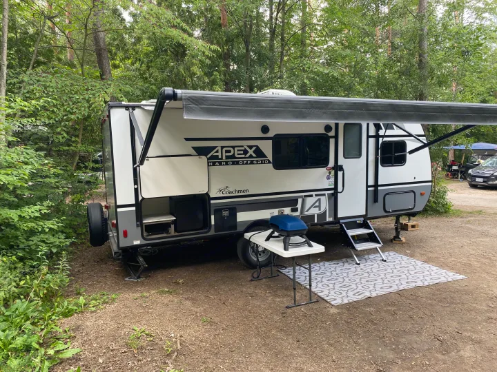 An Apex Nano rv rental sits on a rustic campsite with its awning extended, featuring a grill and steps. Perfect for nature lovers.. Coachmen Apex Nano 194 BHS 2021