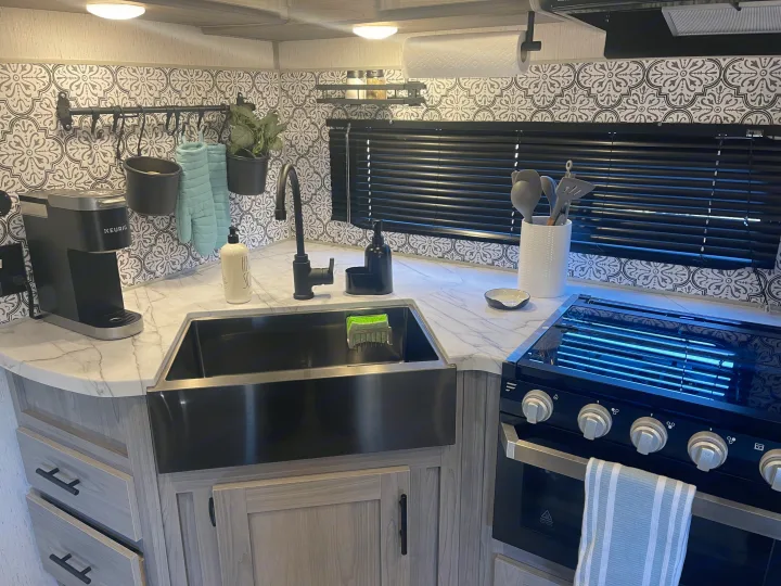 Stylish RV rental kitchen: black farmhouse sink, patterned backsplash, Keurig, oven, and light-colored countertops.. Dutchmen Coleman 2022