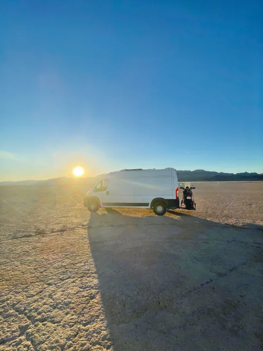 White RV rental van & motorcycle parked on a vast dry lake bed at sunset, mountains in distance. Ideal for adventure.. Dodge Ram Promaster 2500 2017
