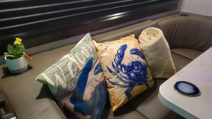 Stylish RV rental interior with gray seating, nautical pillows, a plant, cozy blanket, and agate coaster.. Jayco Redhawk 2022