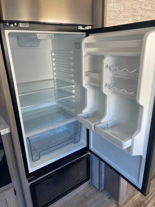Clean, empty refrigerator in an RV rental, featuring glass shelves, door storage, crisper, and temperature controls.. Dutchmen Coleman 2022