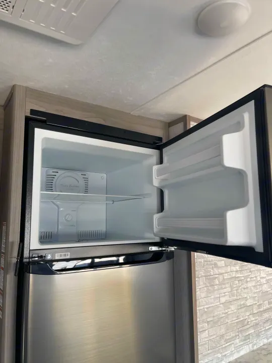 Open, empty two-door refrigerator in an RV rental. Top freezer shows 'Turbo Cooling Frost Free,' with shelves in both compartments.. Dutchmen Coleman 2022