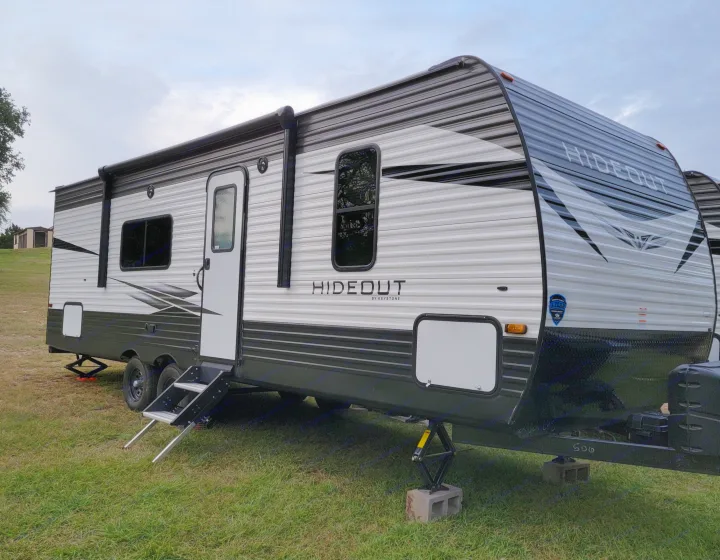 This Hideout by Keystone RV rental is parked on green grass with its steps extended and stabilizers set, ready for camping.. Keystone Hideout 2021