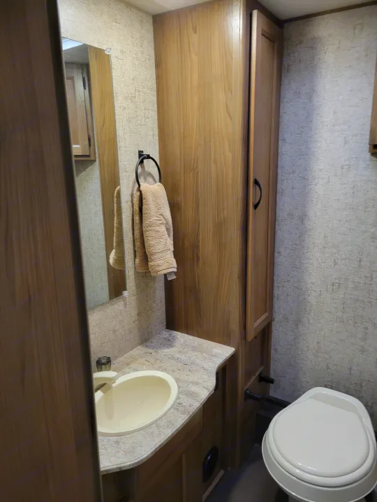 Compact RV rental bathroom features light wood cabinetry, a sink, mirror, and toilet.. Coachmen Freelander 2017