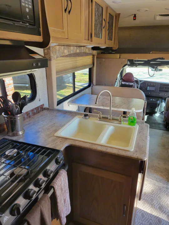 Inside this RV rental: a compact kitchen with stove, sink, microwave, and dinette. Driver's area visible beyond.. Coachmen Freelander 2017