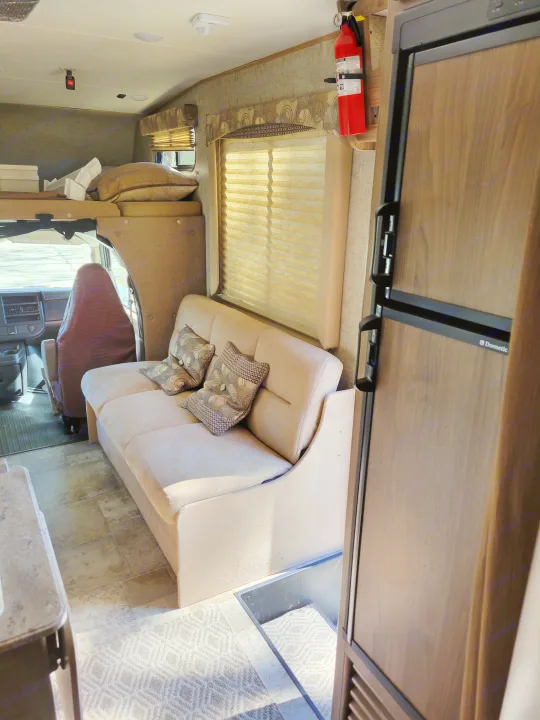 Explore this rv rental's interior: comfy sofa with pillows, large window, Dometic fridge, and spacious driver's cab area.. Coachmen Freelander 2017