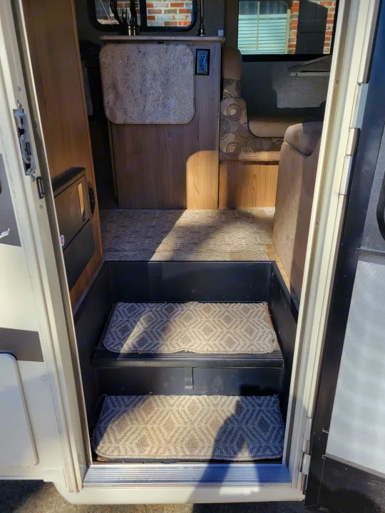 RV rental: View from open door showing entrance steps with patterned mats, leading to the interior dinette and cabinet.. Coachmen Freelander 2017