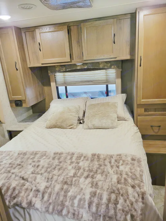 Cozy RV rental bedroom featuring wood cabinets, a comfy bed with a fluffy blanket, and a window with blinds.. Coachmen Freelander 2017