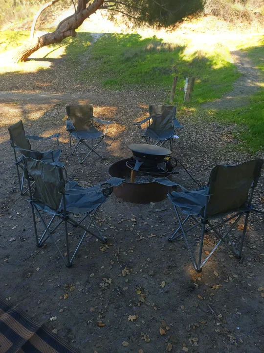 RV rental campsite scene: Portable chairs arranged around a fire pit on dirt ground with leaves, ready for outdoor relaxation.. Forest River Sunseeker 2018