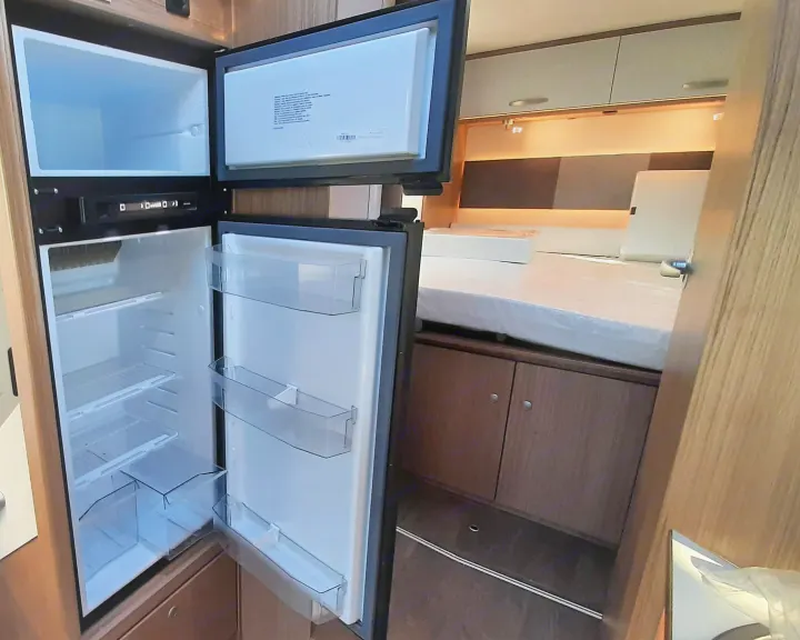 Inside an **RV rental**: Open refrigerator and freezer with controls. A protected mattress and wooden cabinetry are visible.. Carado T459 2022