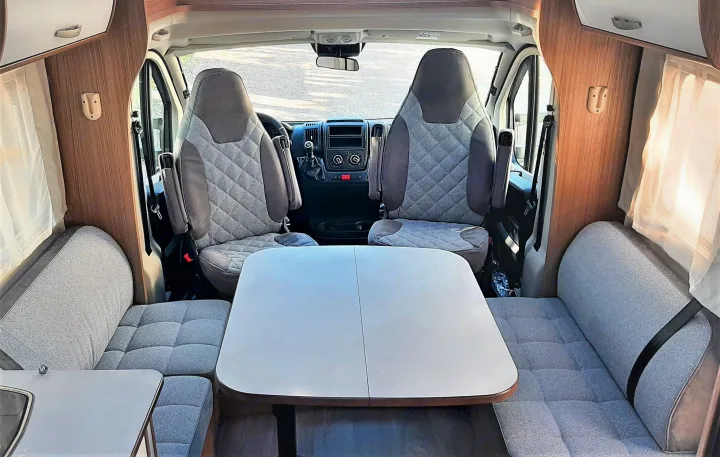 Spacious RV rental interior: swivel front seats, dining area with plush grey upholstered benches & large table.. Carado T459 2022
