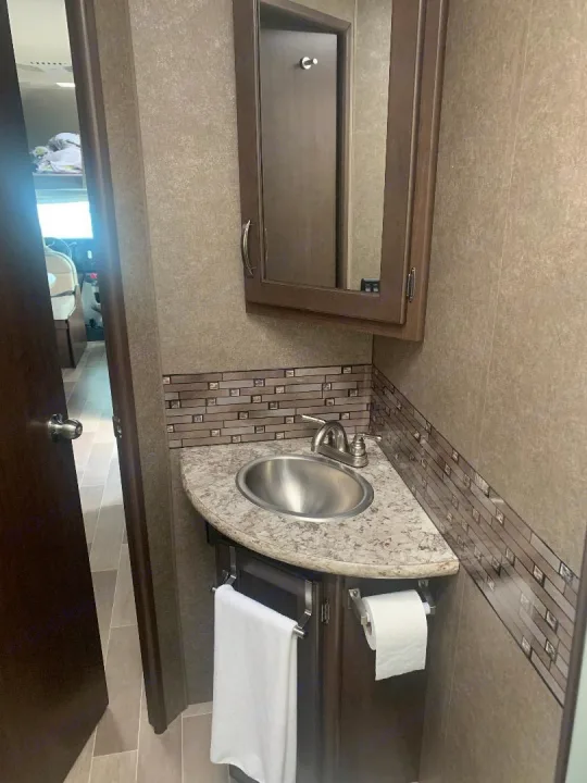 Compact RV rental bathroom with a corner sink, mirrored cabinet, towel, and toilet paper.. Thor Motor Coach Chateau 2020