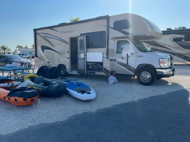 Sunny day with an RV rental parked on gravel. Inflatable boats & paddleboard are outside, ready for outdoor fun.. Thor Motor Coach Chateau 2020