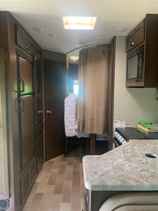 Spacious RV rental interior with kitchen counter, sink, microwave, fridge, and bedroom area with a privacy curtain.. Thor Motor Coach Chateau 2020