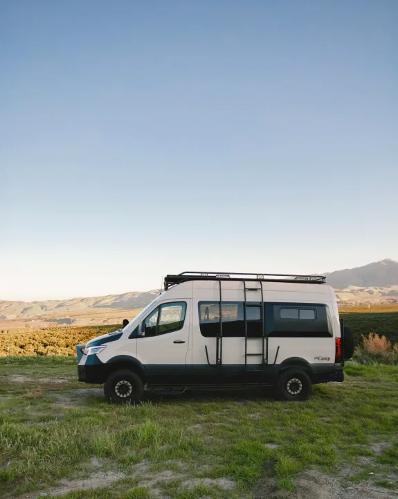Explore van life! This rugged camper van, ideal for an RV rental, is set against a vast, clear sky and rolling hills.. Mercedes-Benz Sprinter 2021