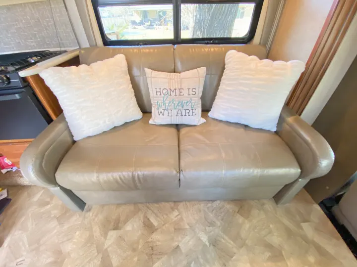 Cozy RV rental living area featuring a beige leather sofa with white pillows and a 'HOME IS WHEREVER WE ARE' pillow.. Jayco Redhawk 2016