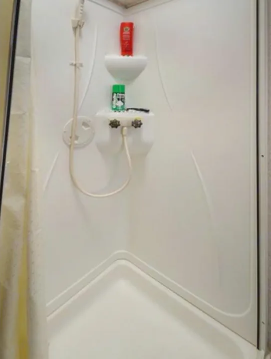 RV rental shower: compact white unit with handheld sprayer, built-in shelves holding toiletries like shampoo.. Forest River Sunseeker 2017