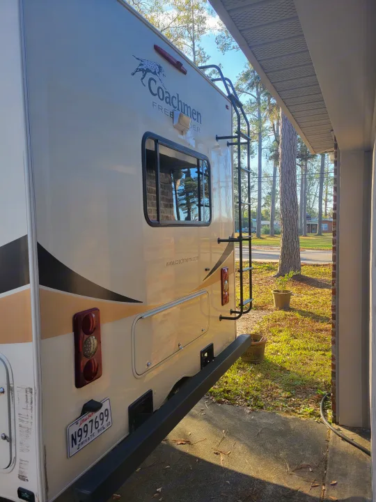 Rear of a tan Coachmen RV, an ideal rv rental, showing its ladder, lights, and Louisiana license plate N997699.. Coachmen Freelander 2017