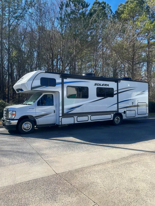 Class C RV rental: A white Solera motorhome parked outdoors, with bare and evergreen trees under a blue sky.. Forest River Solera 2022