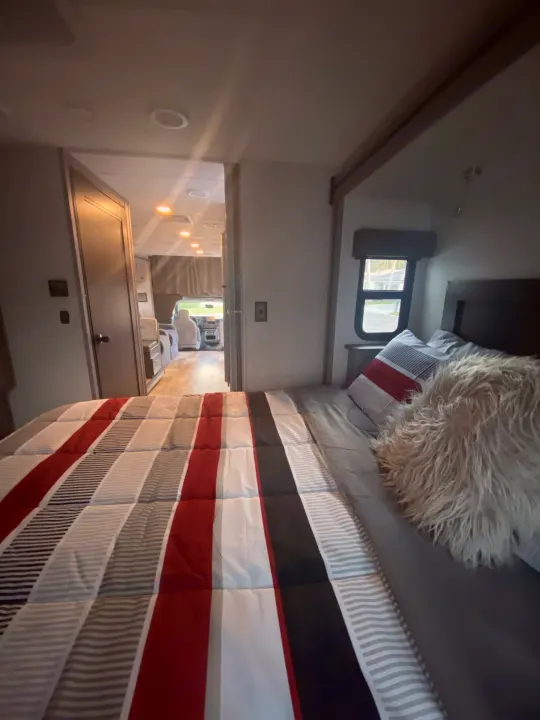 Cozy RV rental bedroom with striped bedding & fluffy pillow. View shows hallway to the driver's area.. Forest River Solera 2022